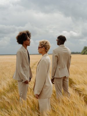 3 person standing in a brown grassfield all wearing suit posing for a photoshoot